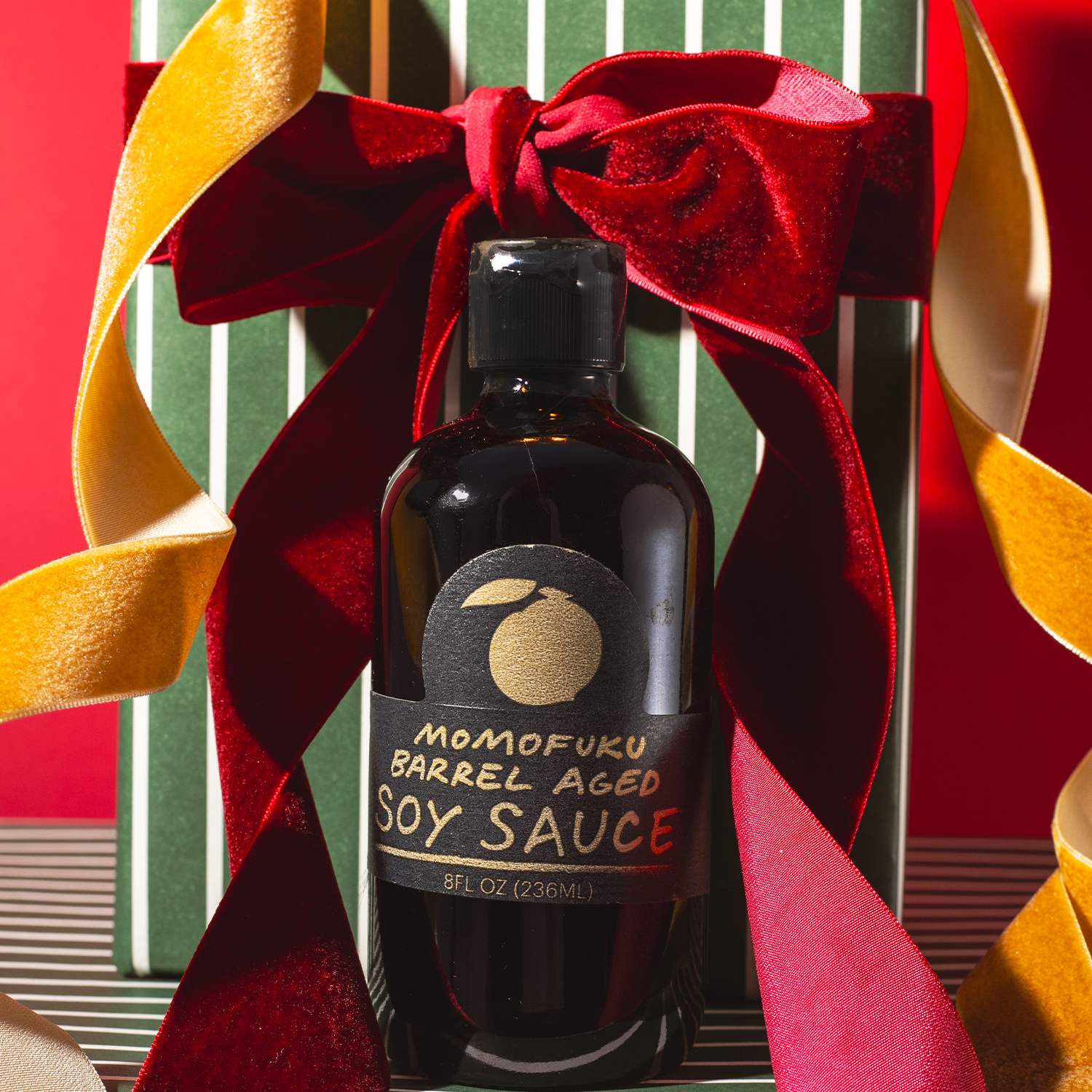 Bottle of Momofuku Barrel Aged Soy Sauce with a red ribbon on a decorative background